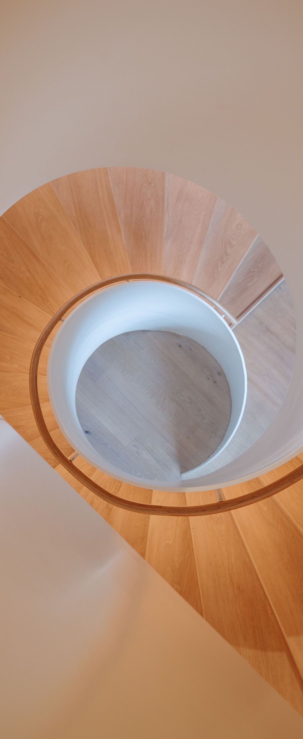An overhead view of a contemporary spiral staircase with a flawless white balustrade and warm wooden steps that elegantly twist downwards, creating a mesmerizing architectural pattern.